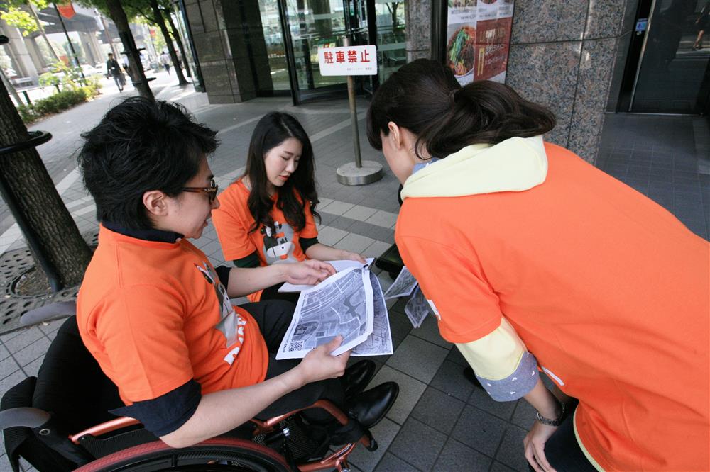 A person on the wheelchair looking for indicators on a map with two other people.
