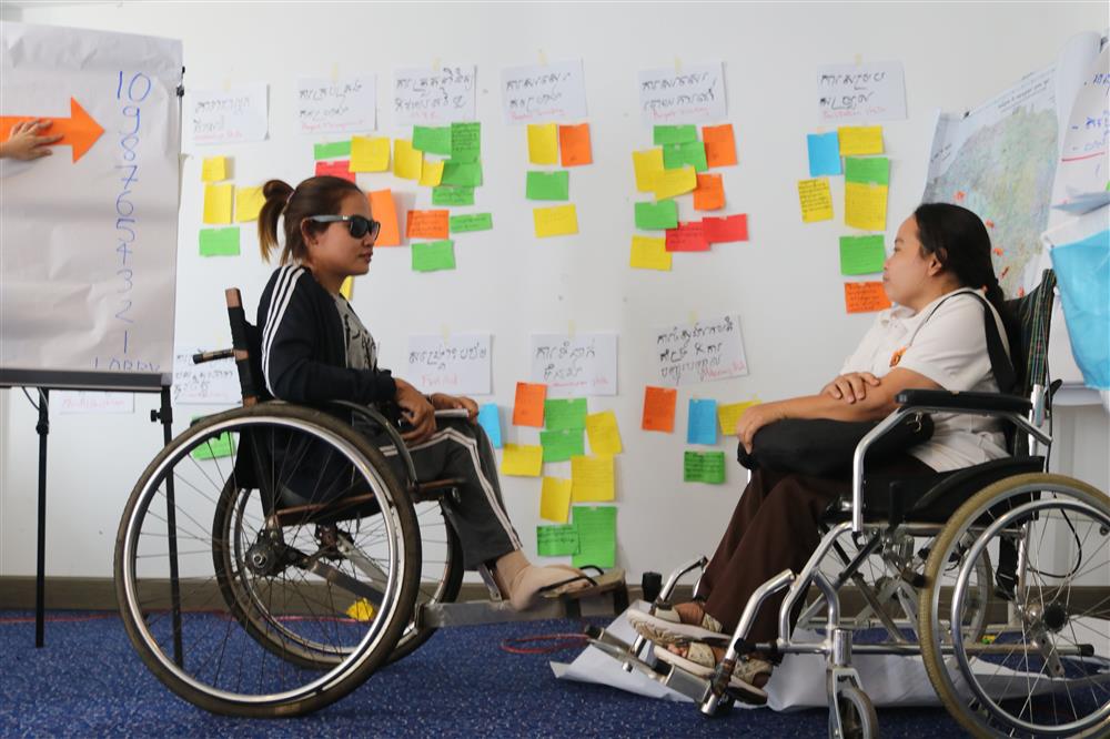 Two women on a wheelchair learning in a workshop.