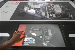 The image shows a hand touching the surface of a touch screen device that depicts a design plan for the Parc de La Villette in Paris with its buildings, parks and streets. 