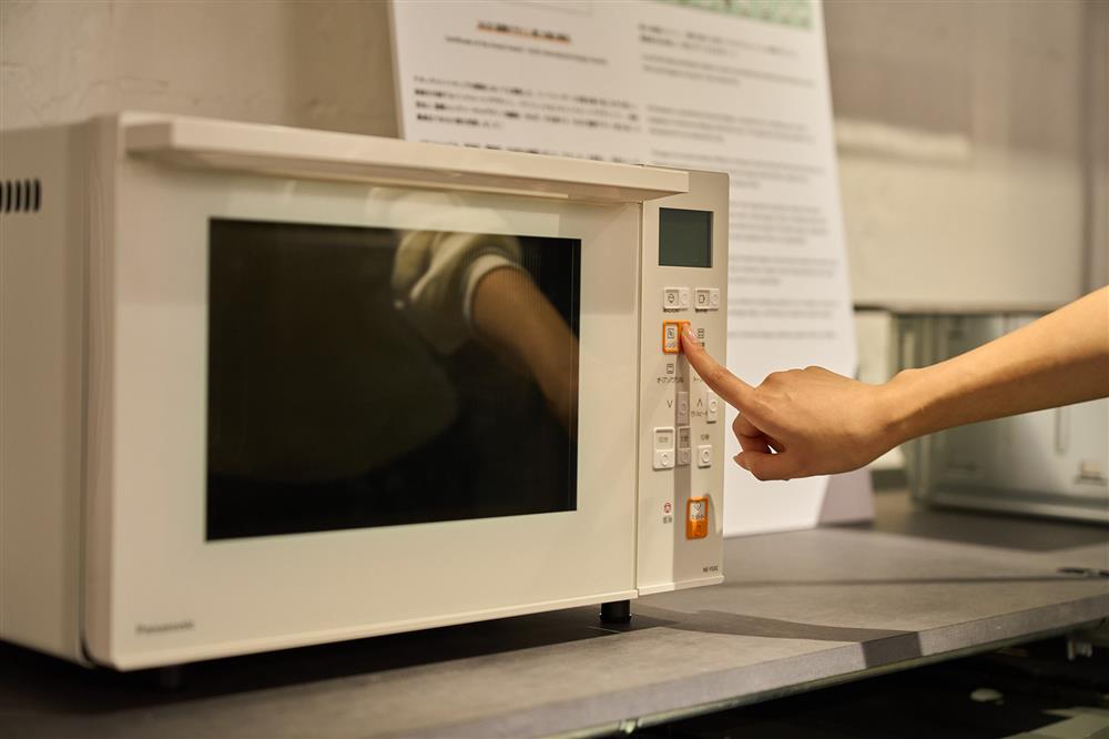 A person’s hand presses a button on a microwave with clear, tactile controls. The image illustrates thoughtful design that makes everyday appliances easier and safer for all users, promoting accessibility and dignity in daily living.