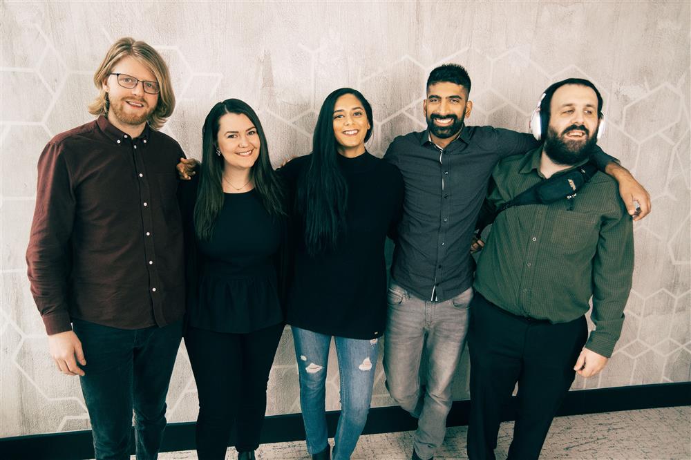 Five Fable team members smile and laugh with their arms on each other’s shoulders.