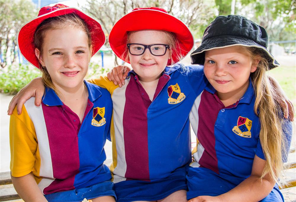 Three girls are hug and smile at the camera, while wearing their uniforms. 