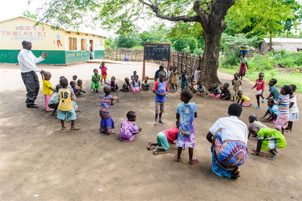 Many children take a class outside a CBCC under a tree.