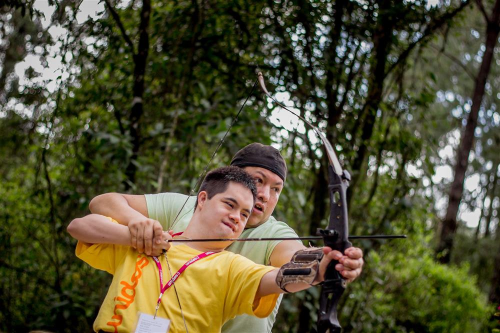 A young volunteer teaching archery to a person with disabilities.