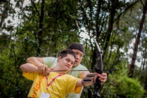 A young volunteer teaching archery to a person with disabilities.