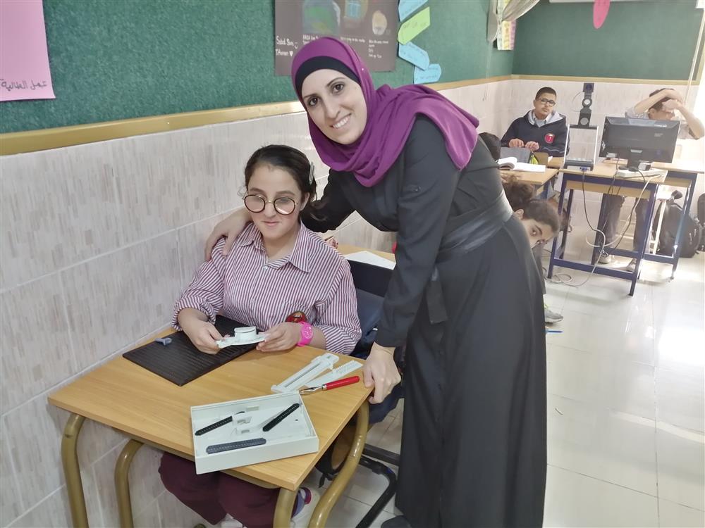 A women holds a girl with disabilities, who is sitting in class by her shoulders.