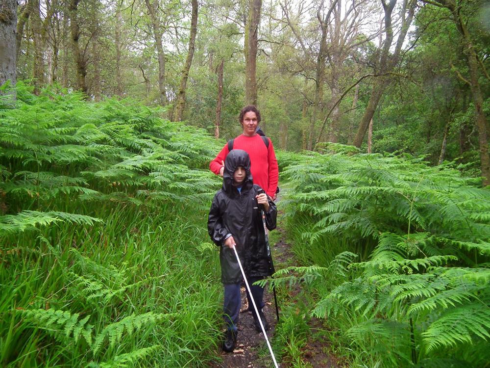 A boy with visual impairments being trained to famiilarise with his surroundings in the woods.