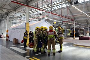 Firefighters and emergency personnel gather inside a transport depot for a safety drill. Their teamwork, diversity, and preparedness highlight collective responsibility in protecting all members of society, including those with disabilities, during emergencies.